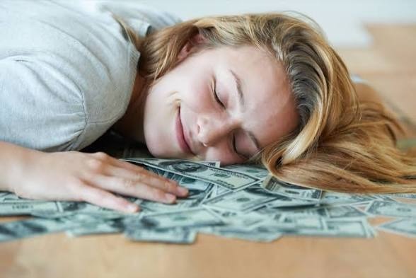 Lady sleeping on the floor covered with money notes and smiling.